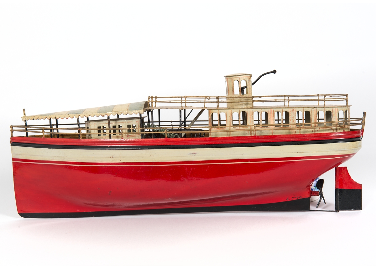 Fartygsmodell. Leksaksbåt av plåt. Rödmålat skrov med svartvitt bälte över vattenlinjen. Rak förstäv, häckakter, roder och en trebladig propeller. Förligt däckshus överspänt med "suntält" av plåt, akterut passagerarsalong, navigationshytt. Propellermaskineriet består av en tvåpolig elektrisk motor driven av ett De Lanche element. Gråmålat skrå.