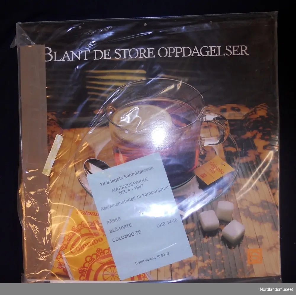 Flere reklameplakater pakket inn i plast. De som vises er: Reklame for Colombo-te med påskriften "Blant de store oppdagelser" og logo for S-laget; og plakat med påskriften " Spør oss om påskemat" og logo for S-laget. Plastforpakningen inneholder også et papir med påskriften: "Til S-lagets kontaktperson. Markedspakke nr. 4 - 1987. Reklamemateriell til kampanjene: Påske uke 15, Blå-hvite uke 14-16, Colomo-te uke 14-16. B-sett varenr. 10 89 02".