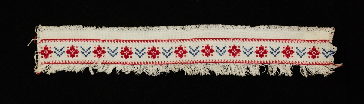 Prov på hyllremsa broderad på 1940-talet.
Motiv/dekor: Korstygnsbroderi i rött och blått.
Birgit Uggla var gift med kammarherre Erik Uggla.