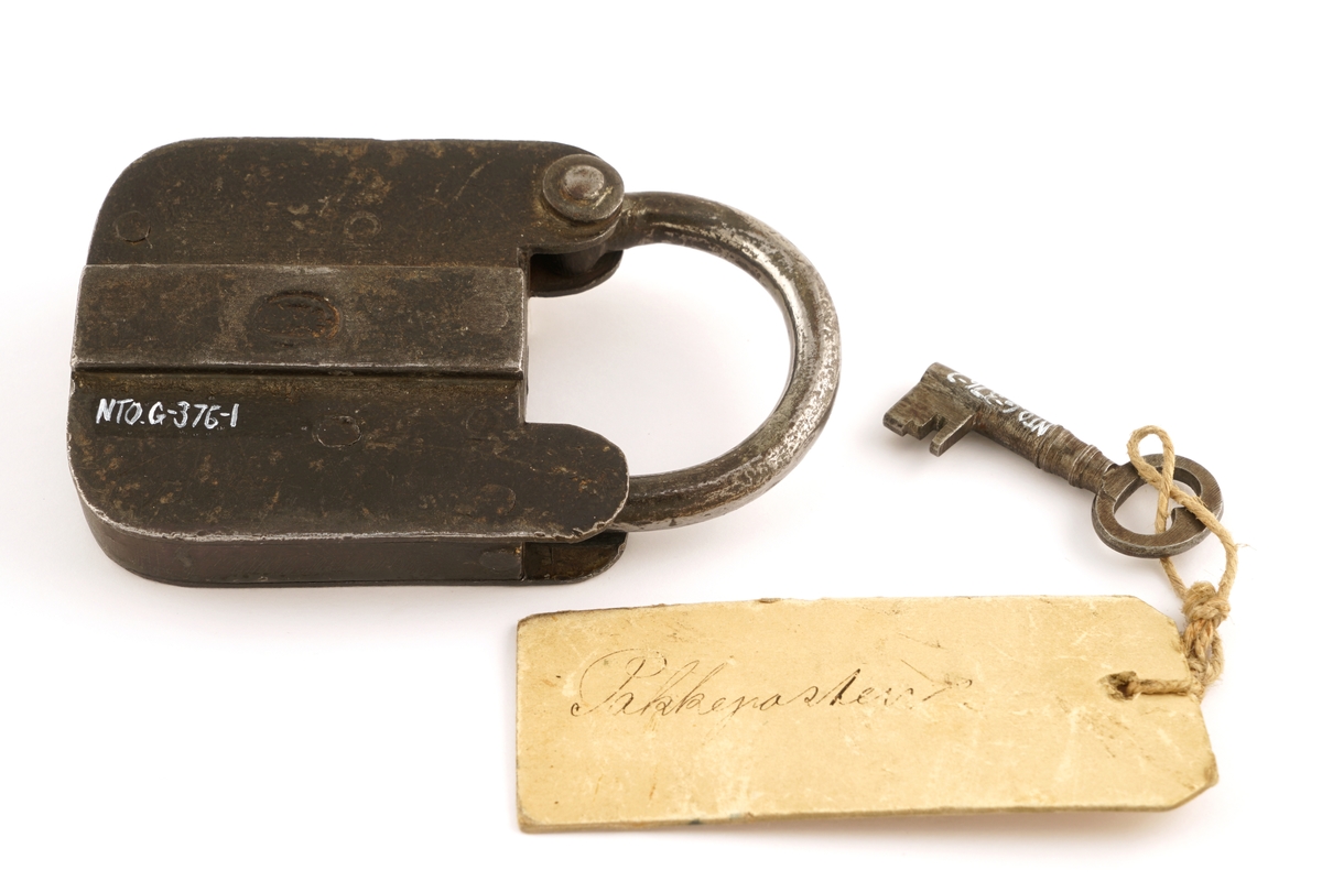 Jern, firkantet, svingbart lokk over nøkkelhullet.
Nøkkel, jern, firkantet skjegg, gjennomboret.
Papirlapp knyttet fast i nøkkel med snor.