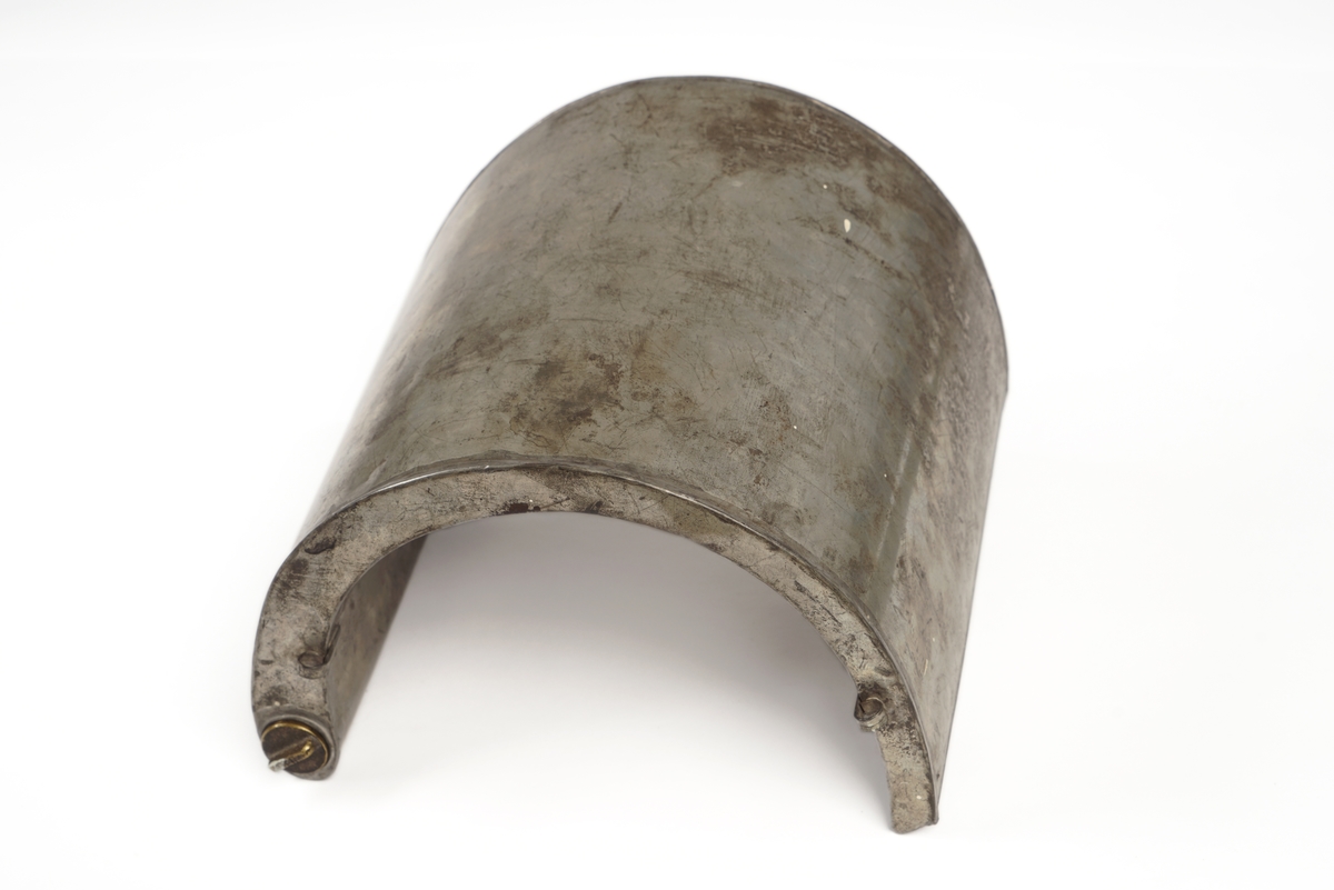 Halvrund blikktank for smugling av sprit eller brennevin. Tanken er utstyrt med hemper på hver sin side, og to steder på toppen for seler. Påfyllingsmulighet på toppen av tanken, med skru-kork.