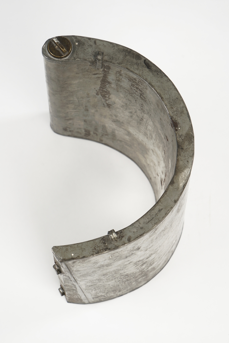 Halvrund blikktank for smugling av sprit eller brennevin. Tanken er utstyrt med hemper på hver sin side, og to steder på toppen for seler. Påfyllingsmulighet på toppen av tanken, med skru-kork.