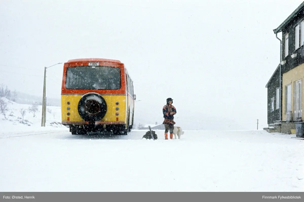 Rutebussen utenfor butikken i Masi (Máze på samisk) på 1970-tallet. Bussen er registrert Y-895. Det var en Volvo B57, karosseri bygd hos Vestfold Bil og Karosseri (VBK), Horten, 1969-modell. Eier av bussen var Finnmark Fylkesrederi og Ruteselskap (FFR) og den er lakkert i selskapets karakteristiske farger, skarp gul og rød. Det er vinter og bussen tar med seg posten innsamlet av postfører Mathis Mathisen Buljo og bringer den videre. En passasjer i kofte, med ryggsekk, ski og trekkhund står utenfor bussen (Se også FBib.10001-033).

Bussen er registrert Y-895. Det var en Volvo B57, karosseri bygd hos Vestfold Bil og Karosseri (VBK), Horten, 1969-modell. Eier av bussen var Finnmark Fylkesrederi og Ruteselskap (FFR) og den er lakkert i selskapets karakteristiske farger, skarp gul og rød. 

Fotograf Henrik Ørsteds bilder er tatt langs den 30 mil lange postruta som strakk seg fra Mieronjavre poståpneri til Náhpolsáiva, videre til Bavtajohka, innover til øvre Anárjohka nasjonalpark som grenser til Finland – og ruta dekket nærmere 30 reindriftsenheter. Ørsted fulgte «Post-Mathis», Mathis Mathisen Buljo som dekket et imponerende område med omtrent 30.000 dyr og reingjetere som stadig var ute i terrenget og i forflytning. Dette var landets lengste postrute og postlevering under krevende vær- og føreforhold var beregnet til 2 dager. Bildene gir et unikt innblikk i samisk reindriftskultur på 1970-tallet. Fotograf Henrik Ørsted har donert ca. 1800 negativer og lysbilder til Finnmark Fylkesbibliotek i 2010.
