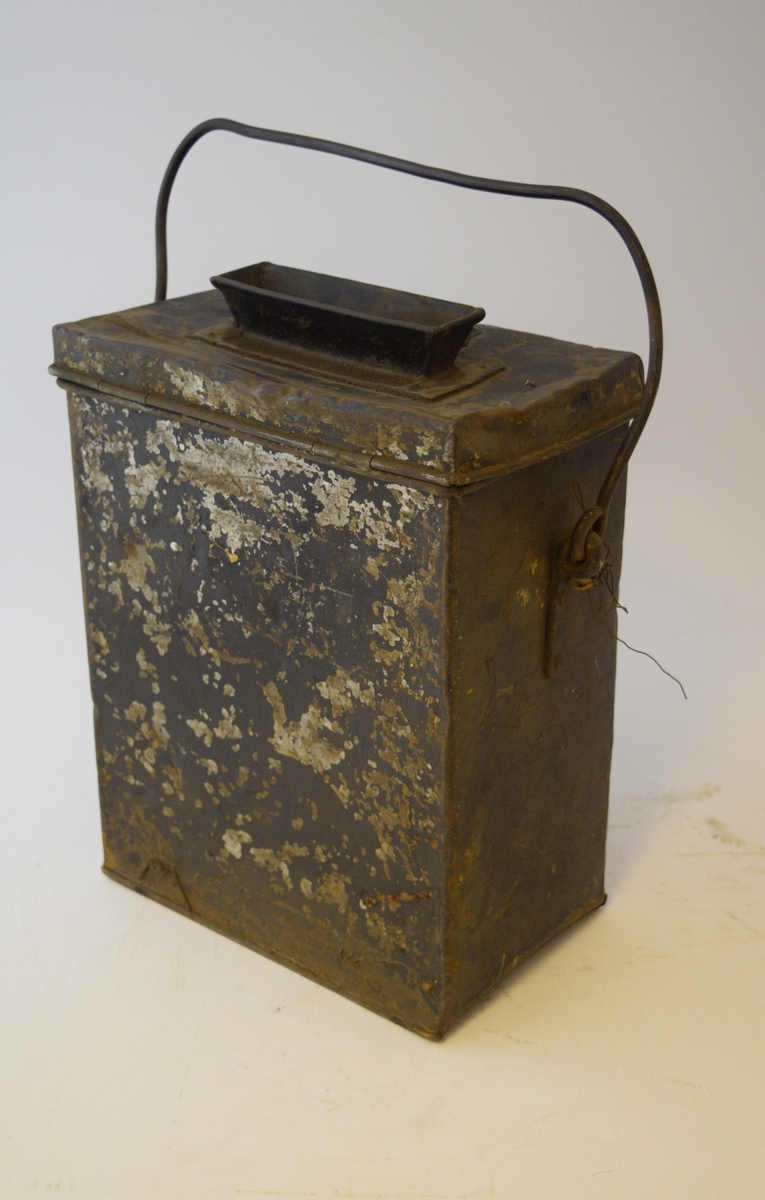 Firkantet kasse med lokk festet med hengsle og hengelås. Smal rektangulær åpning midt i lokket med trakt. Hank festet på sidene.