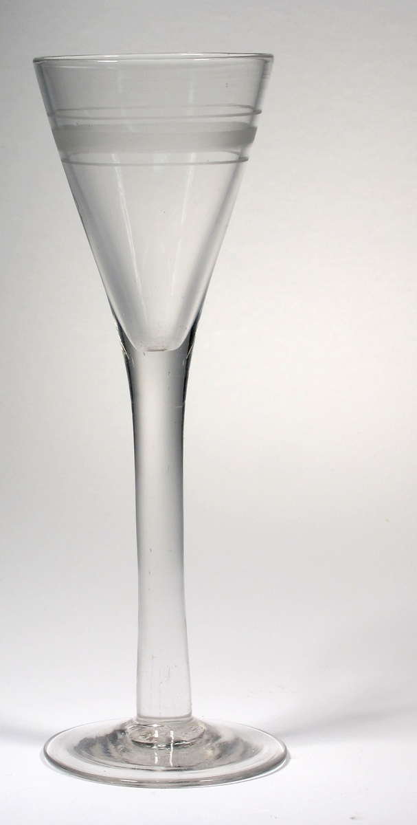Spetsglas.
Heldraget ben, skivfot.
Dekor i form av en bredare och två smala matta ränder i överdelen av kupan.
Ofärgat klarglas.
Ovan angivna mått avser övre diameter.
Fotdiameter: 51 mm.
Inskrivet i huvudkatalogen 1980.