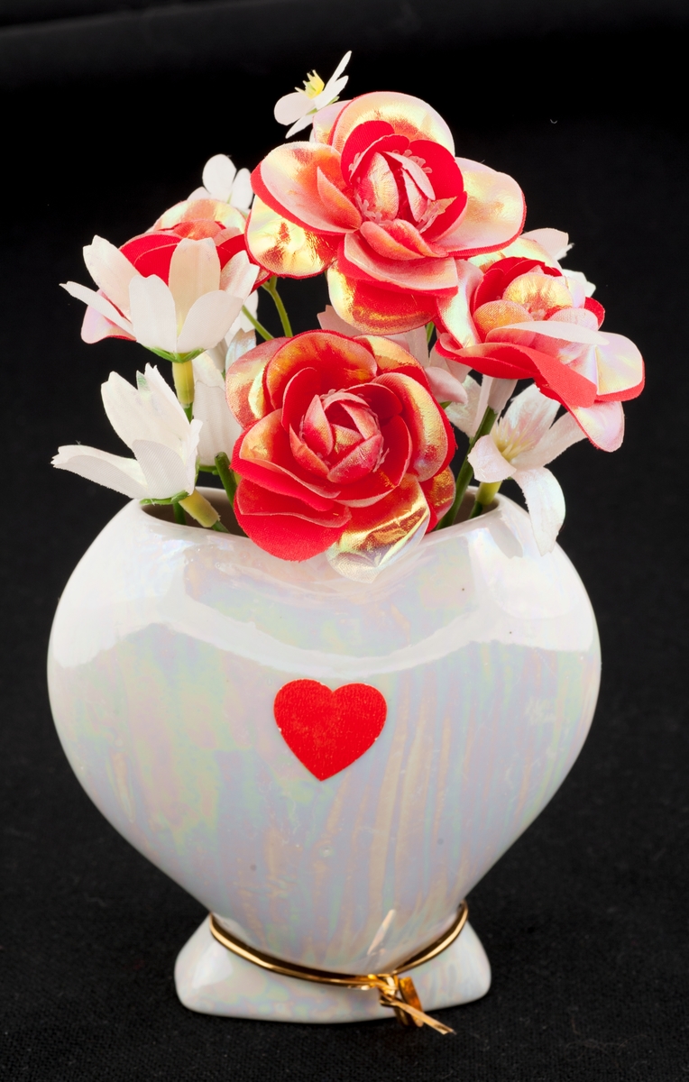 Hvitt hjerte med små røde og hvite blomster i plastikk oppi.
