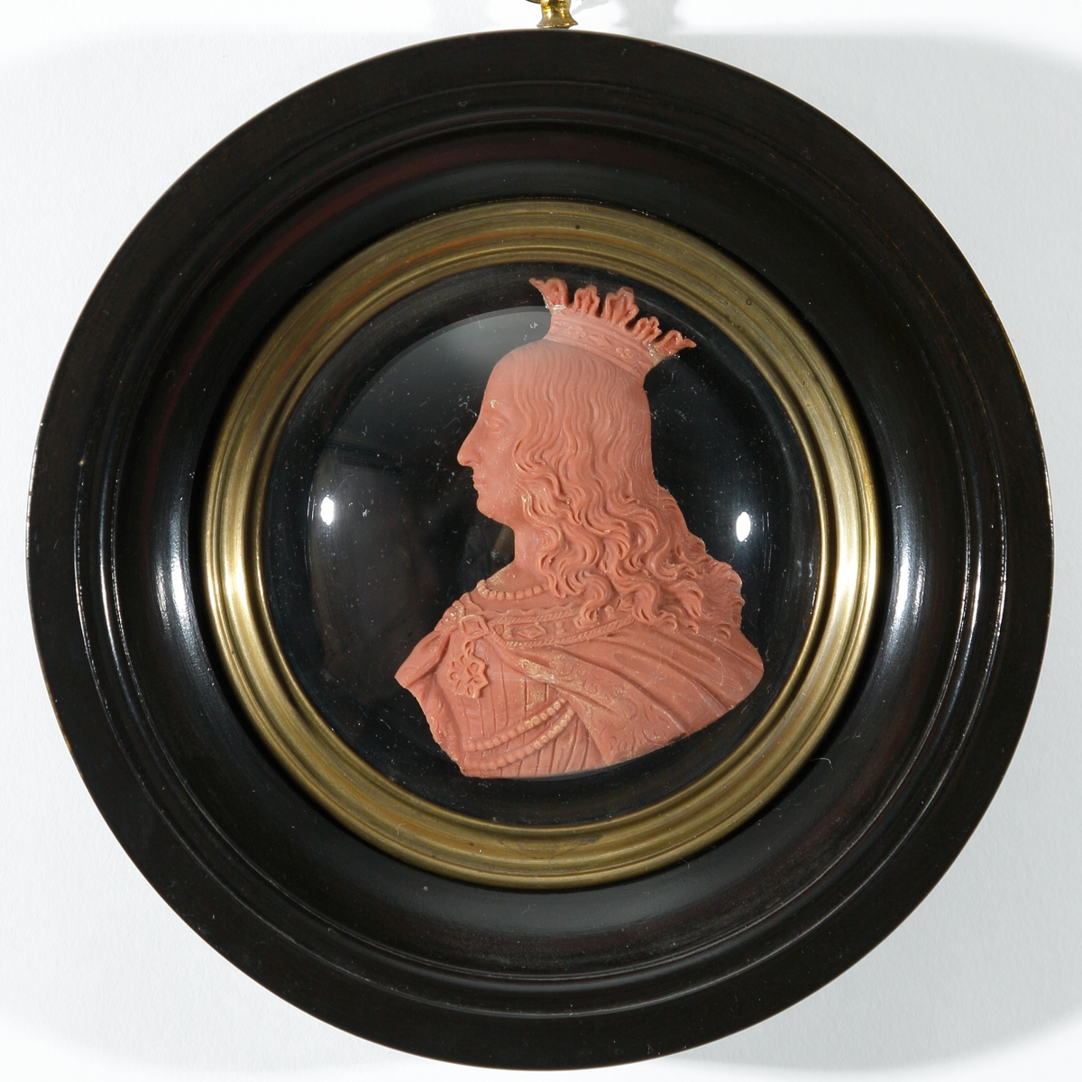 Vaxtavla. 
Reliefporträtt i profil (bröstbild), utfört i tegelrött vax. Föreställer drottning Margaretha (1352-1412) (fantasiporträtt) . Inramad i rund, profilerad och svartlackerad träram med en rund, konvex glasplatta över själva porträttet, fastsatt med mässingslist.
På bakstycket klistrat papper med förklarande text om drottning Margaretha och längst ner tillverkarens namn och adress: "A. Salmson. boende vid Mynttorget. Huset No 1". Upphängningsring i mässing.