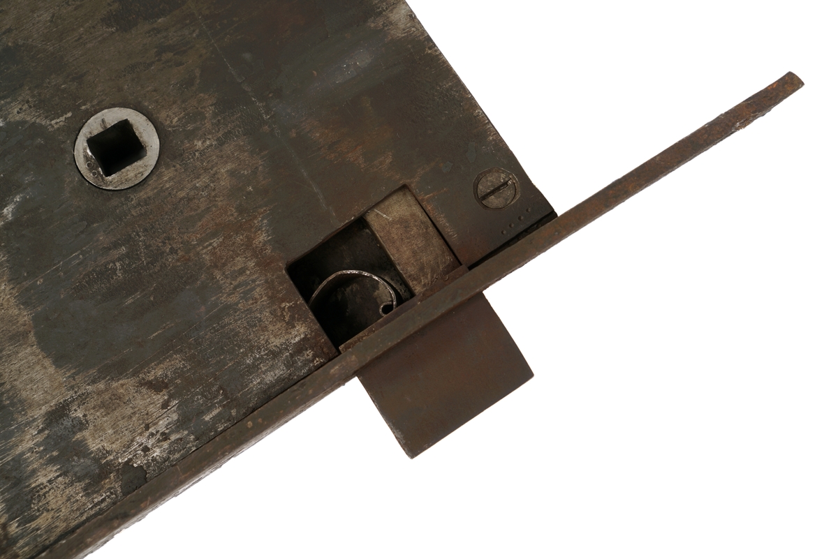 Dørlås for innmontering i dør av jern. Det medfølger tre monteringsbraketter, som selve låsen har vært montert på. Låskassen er rektangulær, med avrundede hjørner på den ene siden, og et større, flatt jern på den motsatte siden.Nøkkel følger med