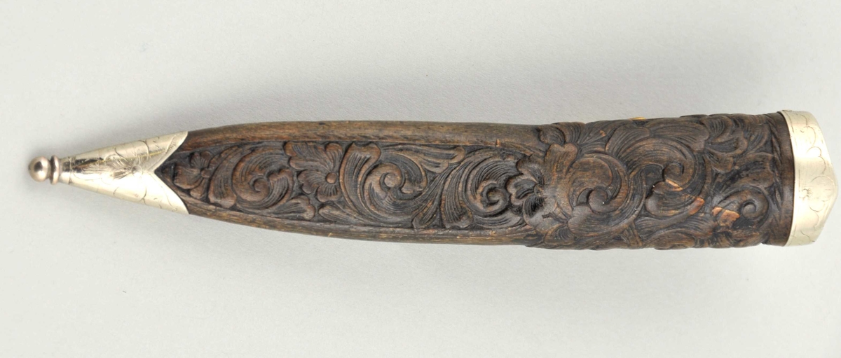 Slir av svart geitehorn med sylvholkar. Sliri har skorne rosur, og holkane er graverte. Hempa er regulerbar med spenne. Kniven er burte, men har hatt holkar av nysylv og skaft av runnen løn.