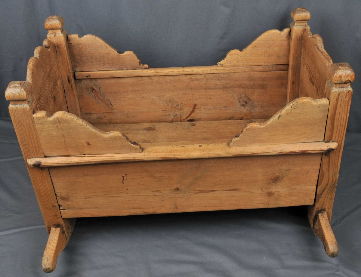 Vogge med nedslitne meiar. Botn er sett saman av 3 bord som ligg lause. Toppen av endeveggane, samt sidekantane er utskorne i bogeformer. Stolpane er firkanta med enkle, utskorne kuler på toppen. Vogga er noko slarkete og slitt.
