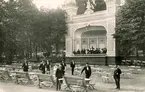 Musikpaviljongen vid sommarrestaurangen Tivoli med musikkår på estraden samt serveringspersonal vid parkmöblerna. Vykort.