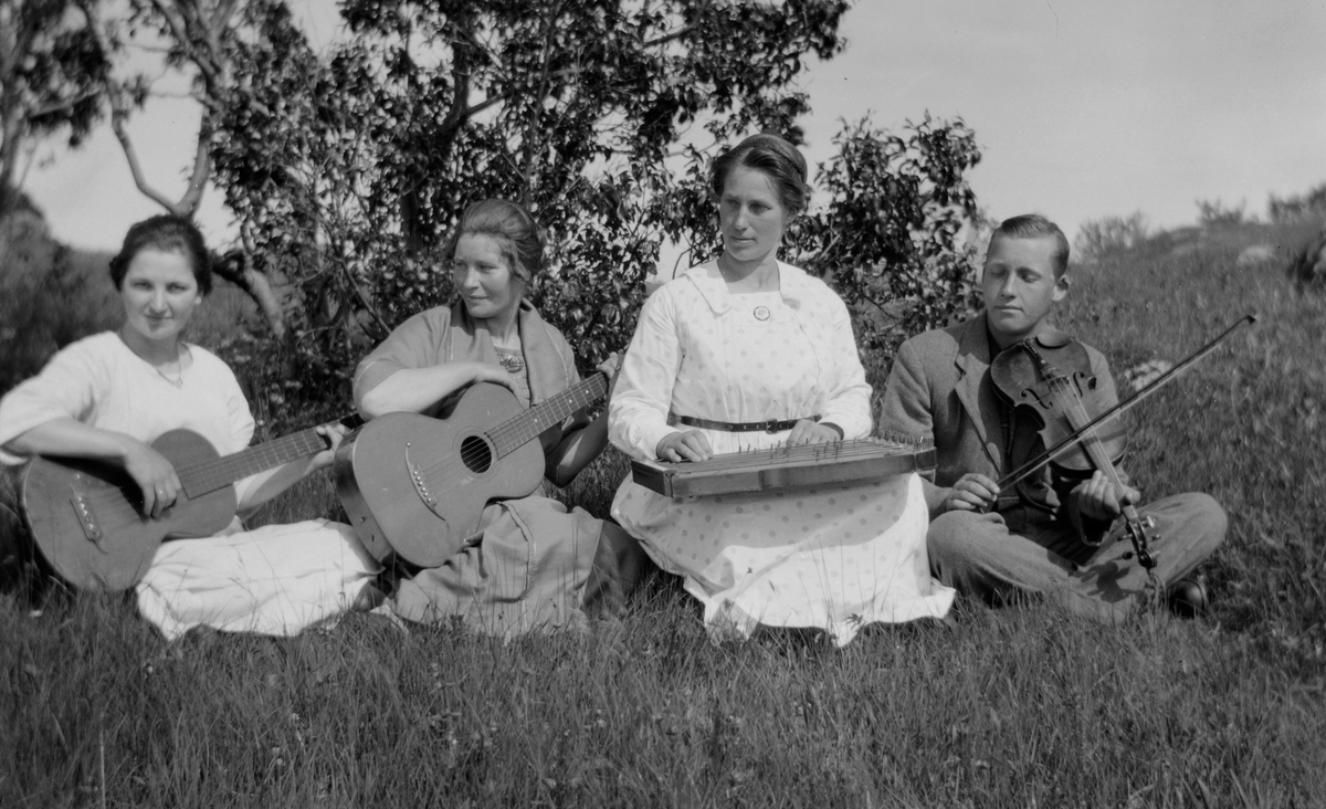 Kvinner og Mann sitter i gresset med instrumenter.