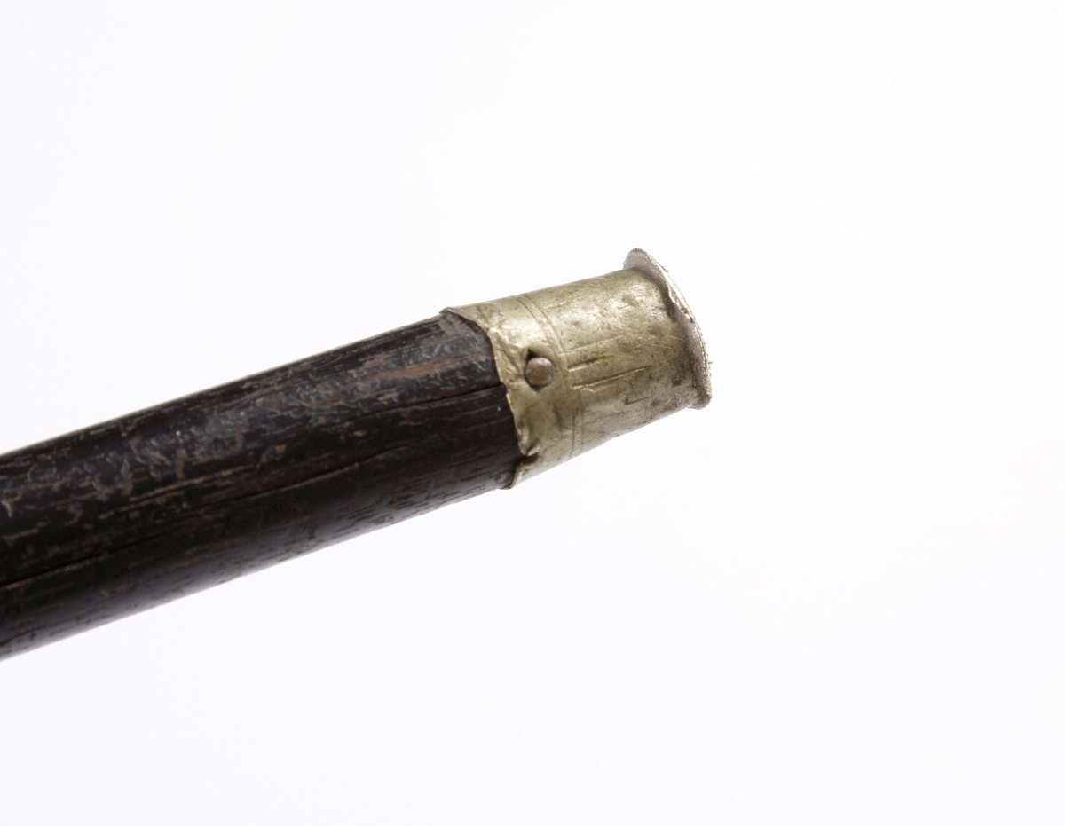 Käpp, s.k. spatserkäpp.
Svarvat, svartlackerat trä. Krycka och skoning av silver. Kryckan försedd med gravyr i nyempire och monogram: "A.A.". Stämplar (något otydliga) längs nedre kanten av kryckan.