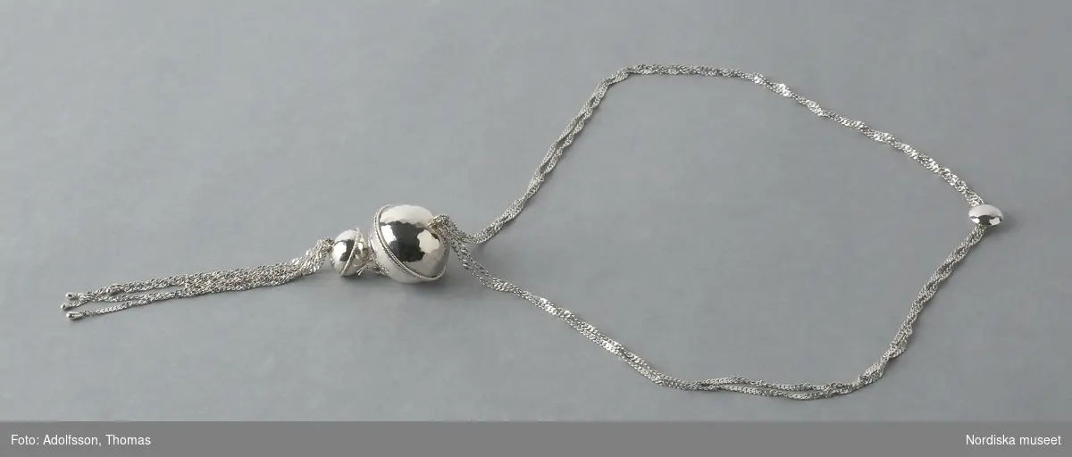 Hängsmycke av silver, "Moder jord" 925/2000, på dubbel silverkedja av platta länkar, spiralformad. Hängsmycket bestående av ett större och ett mindre klot, sammansatta med öglor av tvinnad silvertråd, det större klotet överst. Det mindre klotet avslutas nedåt med sex löst hängande kedjor av olika längd, spiralformade av samma slag som halskedjan.

Graverad på den större silverkulans nedre halva är Rosa Taikons signatur, samt silverstämplar.
/Helena Lindroth & Petrine Knight, 2014-02-18