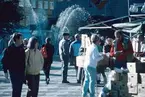 Torghandel på stor torget med fontän i bakgrunden.