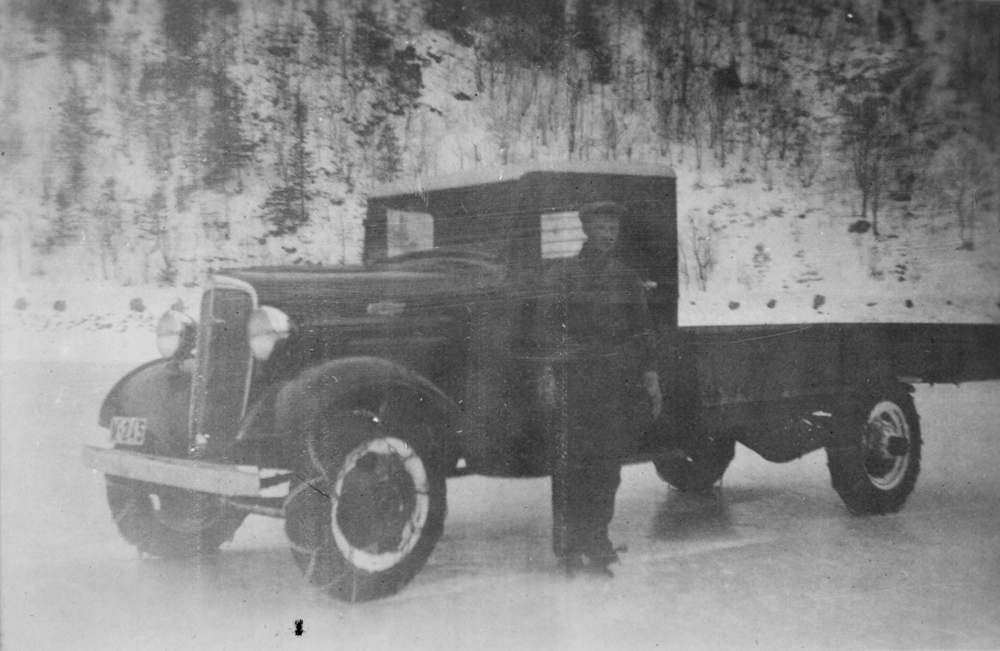 Mann med lastebil på isen på Storbjørnvatnet.
Sannsynligvis i 1936 da det var skøyterenn.
Mannen har skøyter på føttene.
Chevrolet 1936-modell.