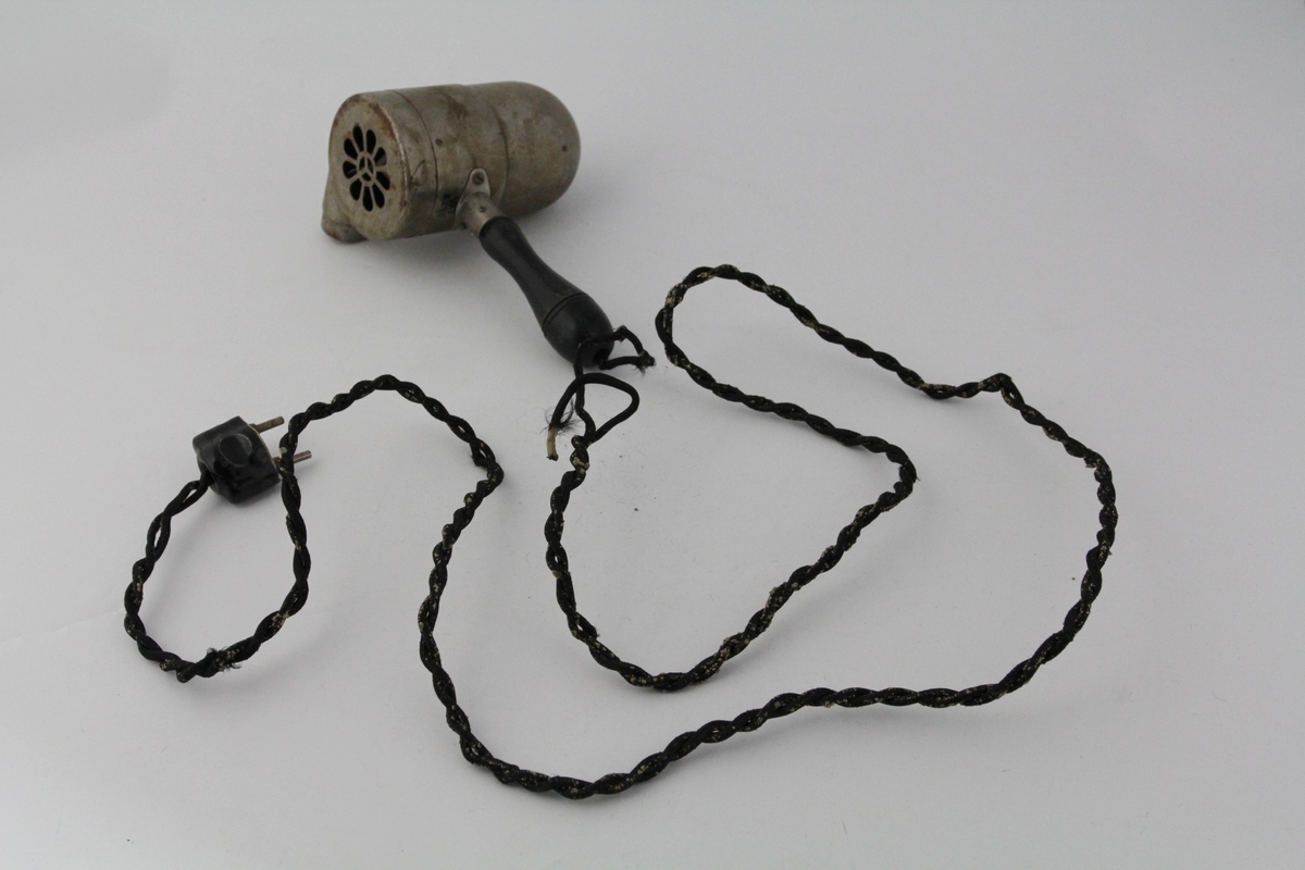 Sylindrisk del med stanghåndtak på undersiden. Utskåret rosettmønster i front, vifte inni. Side v/front: utstikker. Bakside buer inn mot bryter. Ledning går ut fra nedersiden av håndtaket, kontakt i enden. Metallring for oppheng på oversiden av sylinder.