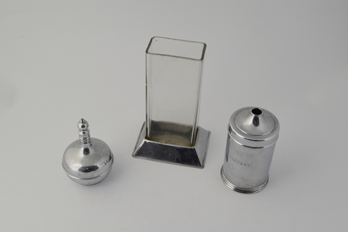 3 stk. beholdere. a) høy rektangulær beholder av glass med løs metallfot. b) sylinderformet med lokk med hull i, inneholder bomullsdotter. c) Flakong, sirkulær med smal lang hals.