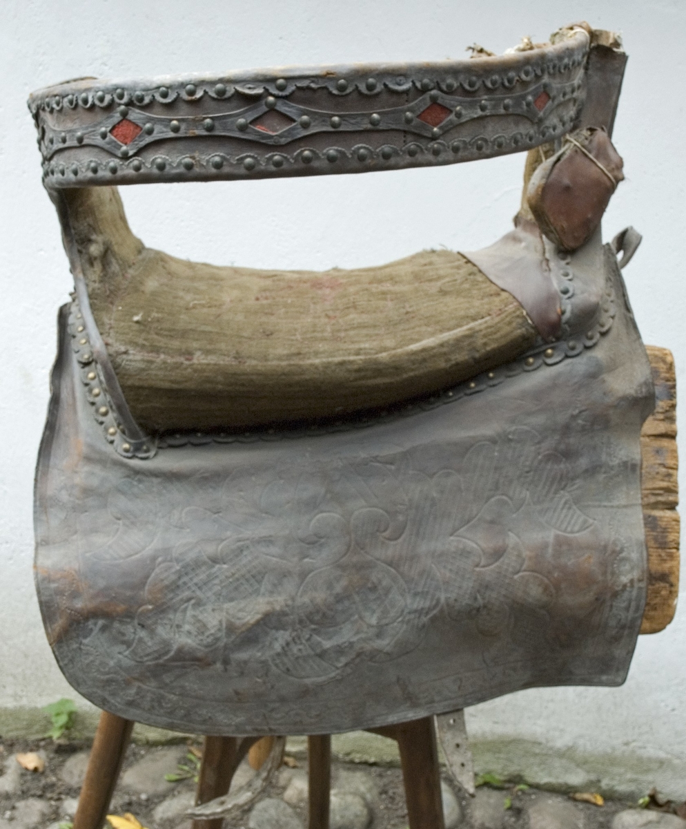 Brudsadel, handgjord. Modell där den ridande färdas sidledes, med fötterna på samma sida på ett fotstöd. Försedd med ryggstöd.
Stomme av trä. Sitsen, sido- och ryggstöden stoppade och klädda med grön ylleplysch, nersydd i mönster med röd tråd, troligen av lin. På utsidan är stöden klädda med brunt skinn, plåt och nitar. Både plåt och skinn har genombrutna partier, med underliggande rött kläde. Märkningen GTDR (osäker) samt 1809 är utskuret i plåt med rött kläde under. Detta är placerat på bakre sidostödet. På båda sidorna hänger stycken av läder med rundade hörn, med präglat mönster som liknar en blomsteruppsättning av barocktyp. Fotstödet hänger på vänster sida, i justerbara remmar av läder med söljor av metall. Trästommen är också stoppad ned mot hästryggen, och klädd med säckväv av jute. Det finns också remmar för fastsättning av sadeln, men de är korta och måste skarvas. Allt trä klätt med målad säckväv.