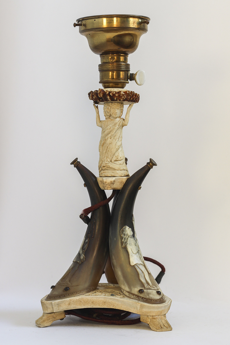 Lampe av kuhorn og bein,kuppel av glass, lampeholder av messing. Akantusmotiv på foten- tre føtter utformet som kløver. Menneskeskikkelser på fot og søyle.