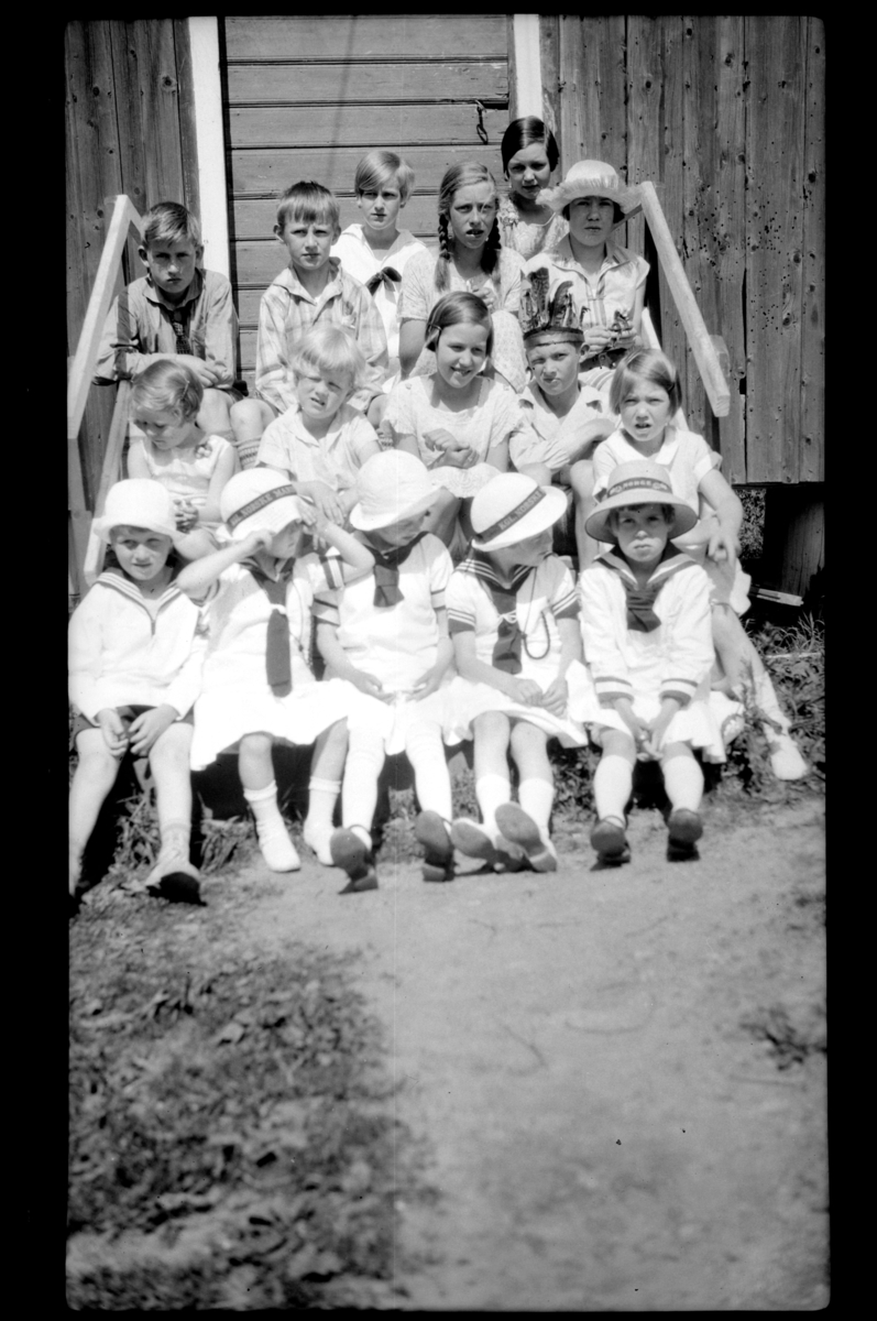 Mange unger sitter på en trapp sammen med Julius Sundt som sitter øverst i trappen. Fotografert 1927.