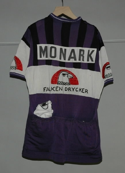 Cykeltröja i vit och lila syntet märkt: "MONARK". Tre fickor på ryggen, märkt: "MONARK" och "FALKEN DRYCKER" på både fram- och baksida. Även "Falkens" logotype på ärmarna.
Med tillhörande monarkkeps och en handske i bakfickor på tröjan.