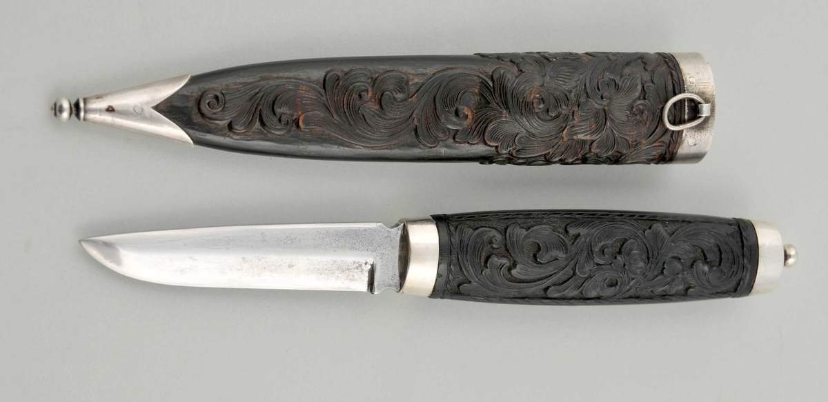 Kniv med utskore skaft i ibenholt og slette holkar, på toppen ei støypt kule.
Slire av horn, utskoren på begge sider, holkar av stål. Knivbladet er eit intstrumentblad, heilstål.
Kniven er orginal, men bladet er avbrote og slipa til på nytt.