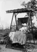 Christine Liljefors med Alf i famnen och Roland bredvid sitter i gungan på strand, sannolik i Sverige, 1905