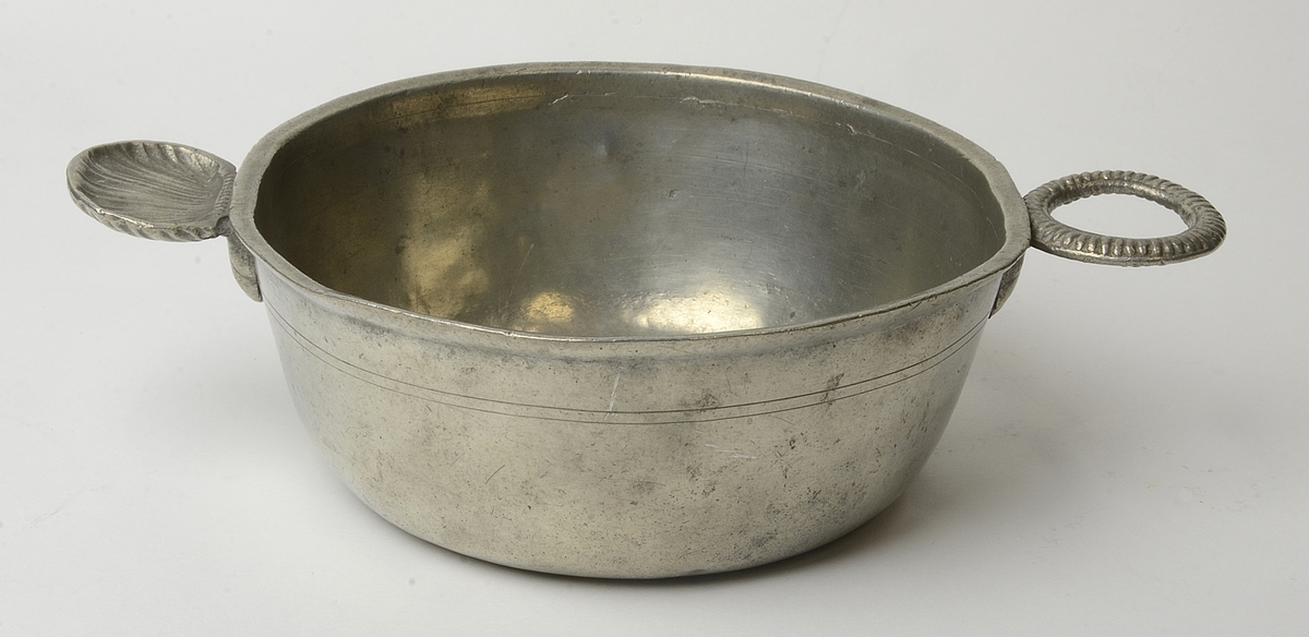 Skål av tenn med handtag i form av snäcka och godronnerad ring.