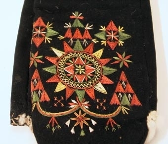 Svarta vinterkyrkvantar. Skinnfodrade med renskinn. Broderi utfört i stjälkstygn, plattsöm och flätsöm med silkegarn i grönt, brunt, vitt och gult. Inuti handen och på tummen öppningar kantade med mjukt vitt skinn. Öppningarna är till för kunna bläddra i psalmboken.