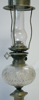 Fotogenlampa med kolonnskaft av slipad och polerad älvdalsporfyr, med fyrsidigt postament. Längs kolonnen löper ornament av brons. Oljehus av slipad kristall, där det sitter brännare av mässing med reglerskruvar. Fäste, möjligen för skärm. Lampglaset är höj- och sänkbart med ett vred.