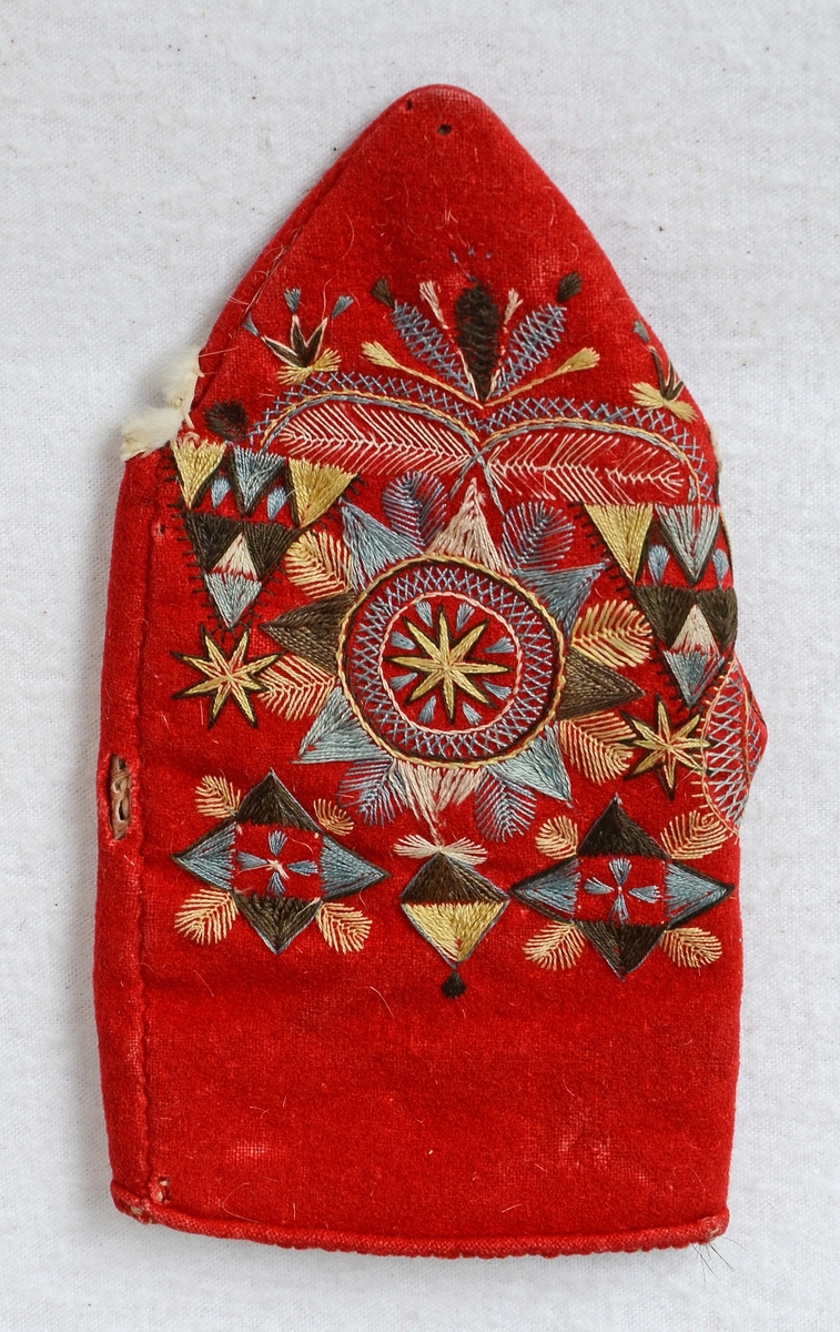 Röd vinterkyrkvante som fodrats med grått skinn. Broderi utfört i stjälkstygn, plattsöm och flätsöm med silkegarn i blått, brunt, svart, vitt och gult. Inuti handen och på tummen finns öppningar, kantade med mjukt vitt skinn, som är till för att kunna bläddra i psalmboken.