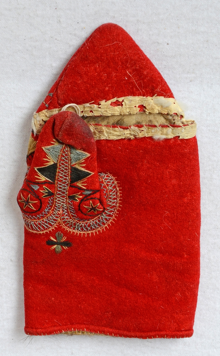 Röd vinterkyrkvante som fodrats med grått skinn. Broderi utfört i stjälkstygn, plattsöm och flätsöm med silkegarn i blått, brunt, svart, vitt och gult. Inuti handen och på tummen finns öppningar, kantade med mjukt vitt skinn, som är till för att kunna bläddra i psalmboken.