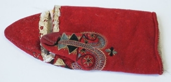 Röd vinterkyrkvante som fodrats med grått skinn. Broderi utfört i stjälkstygn, plattsöm och flätsöm med silkegarn i blått, brunt, svart, vitt och gult. Inuti handen och på tummen finns öppningar, kantade med mjukt vitt skinn, som är till för att kunna bläddra i psalmboken.