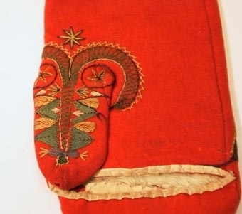 Röd vinterkyrkvante som fodrats med grått skinn. Broderi utfört i stjälkstygn, plattsöm och flätsöm med silkegarn i blått, brunt, svart, vitt och gult. Inuti handen och på tummen finns öppningar, kantade med mjukt vitt skinn, som är till för att kunna bläddra i psalmboken.