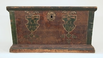 Kista av trä. Kistan avsmalnar nedåt, har plant lock och är brunmålad med gröna hörn och kanter. På framsidan två målade sköldar, den ena märkt: G.R.AN. och den andra BK. 1764. Lockets insida är enkelt målat och märkt ANNO 175 GD.