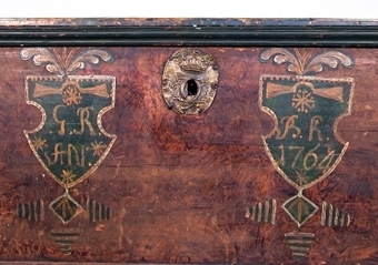 Kista av trä. Kistan avsmalnar nedåt, har plant lock och är brunmålad med gröna hörn och kanter. På framsidan två målade sköldar, den ena märkt: G.R.AN. och den andra BK. 1764. Lockets insida är enkelt målat och märkt ANNO 175 GD.