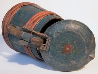 Pipkanna uppbyggd av 14 stavar, med grepe, pip och fällock. Målad i blått och med röda band. På locket samt grepen är blomsterornering i rött, gult och grönt målat.