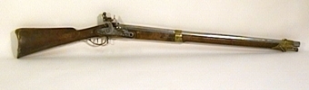 Armégevär med flintlås och räfflad pipa. Piphylsor, v. låsbleck, varbygel och stötbleck av mässing. Ställbart sikte och kolv med snidad slinga på anhållet. Laddstake av järn med mässingsring i knoppen.