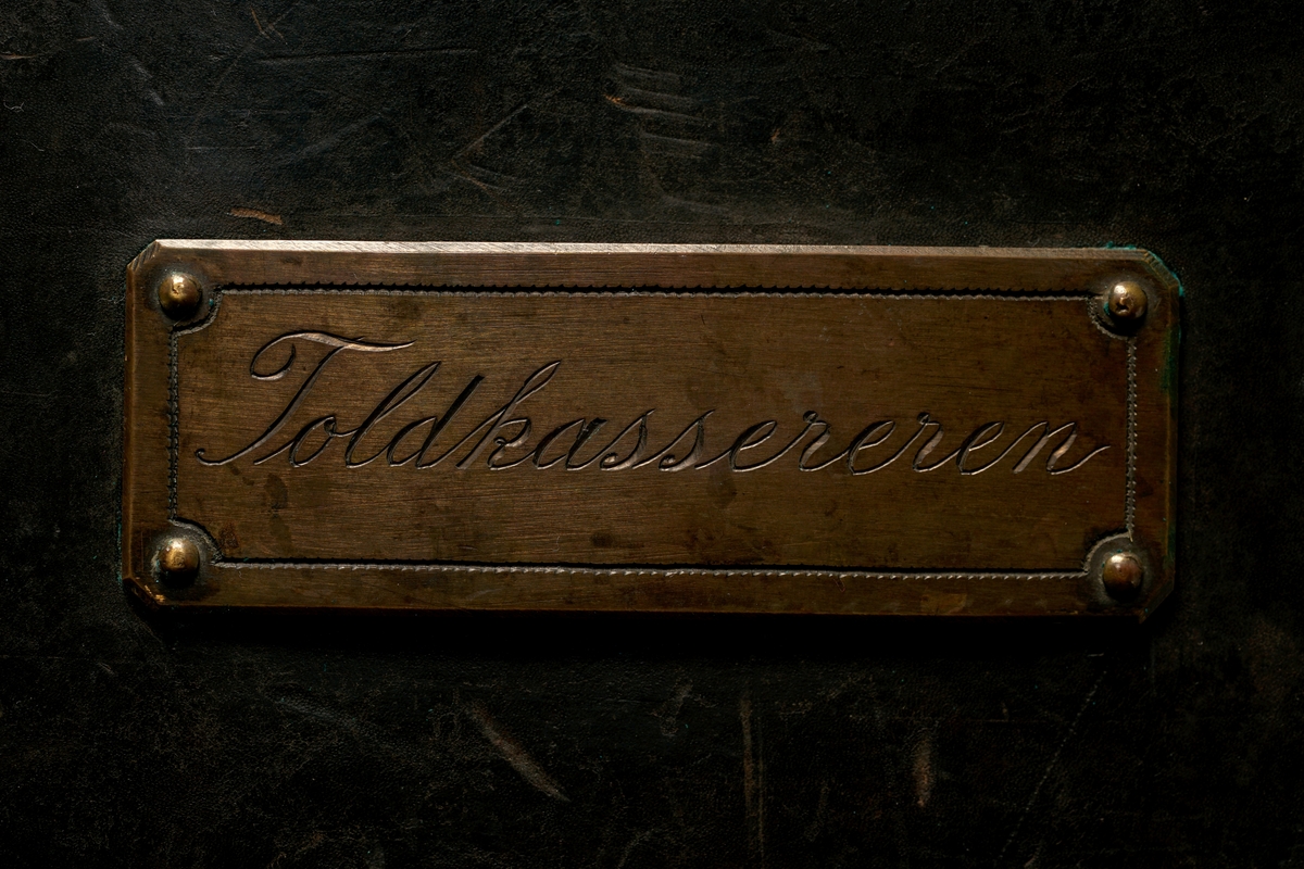 Veske av lær med 9 messingbøyler og to messinglenker for låseanordning. Låsepinne av tre. (Denne ligger i vesken)