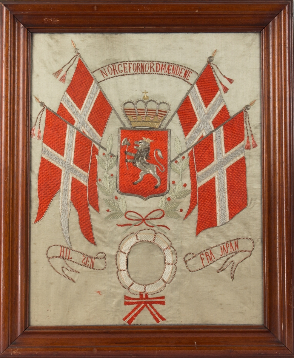 Brodert silkebilde med tekst NORGE FOR NORDMÆNDENE. Midt i motivet norsk riksvåpen med krone omkranset av to norske flagg på hver side. Under brodert livbøye med plass til fotografi/portrett uten at det har vært montert noe bilde.
