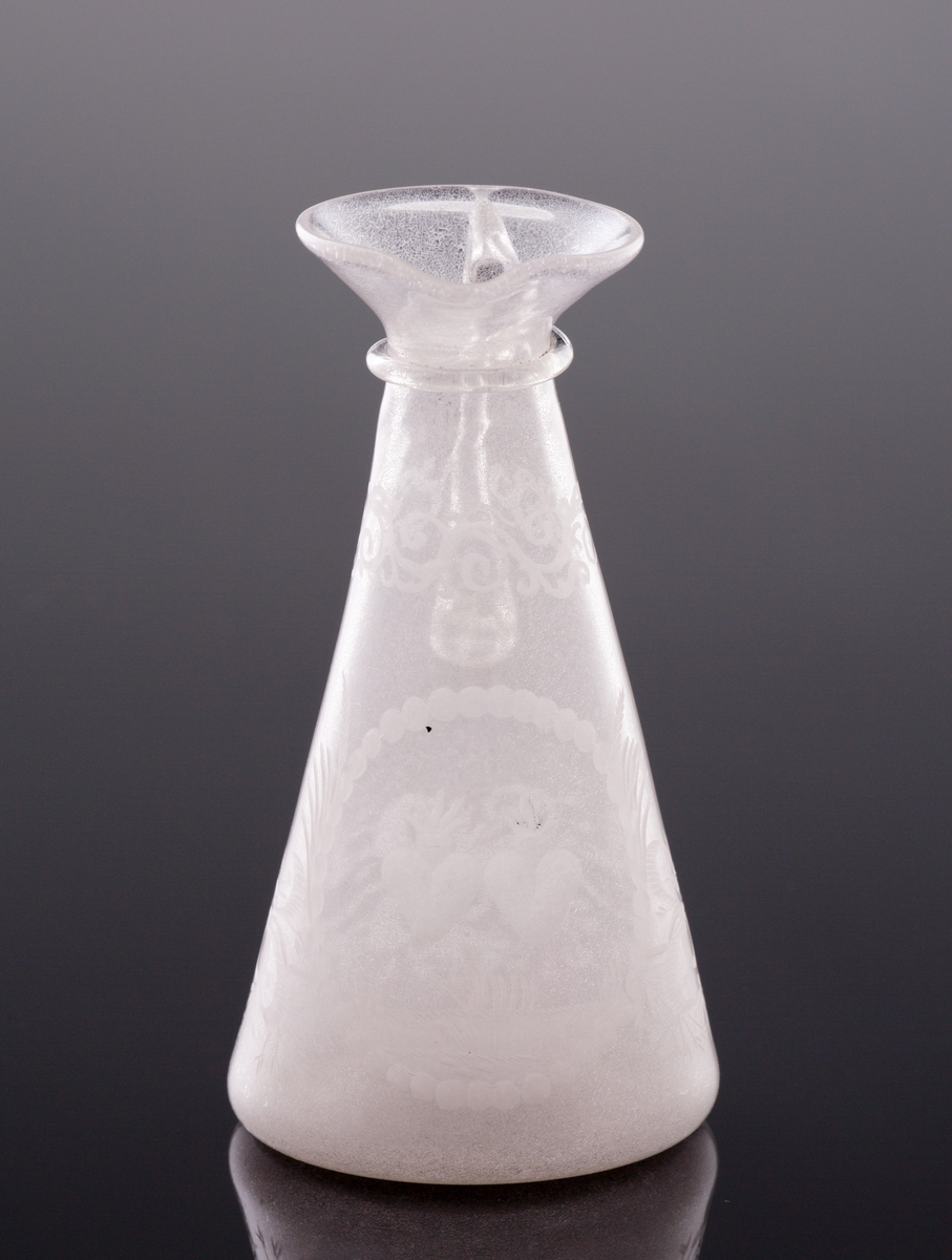 Kanna. 
Konande modell med hänkel och graverad dekor av bladrankor, två brinnande hjärtan m.m.
Mynningen utvikt med en formad pip. Under mynningen en påklippt ring.