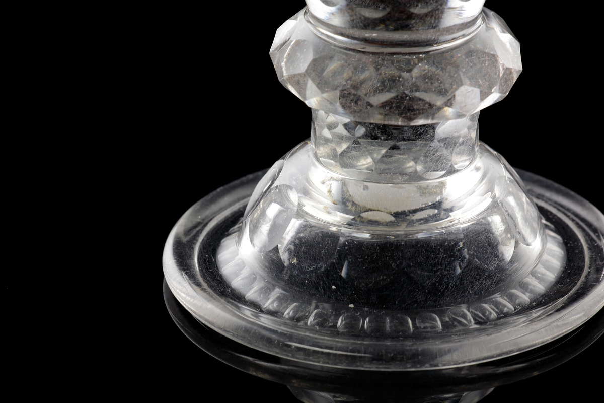 Pokal av glas, med lock. 
Slipat och graverat mönster med kungligt spegelmonogram: "FR"* i kartusch under krona. Invikt kant på foten.

*"FR" (Fredericus Rex= Fredrik I av Sverige, reg. 1720-1751).