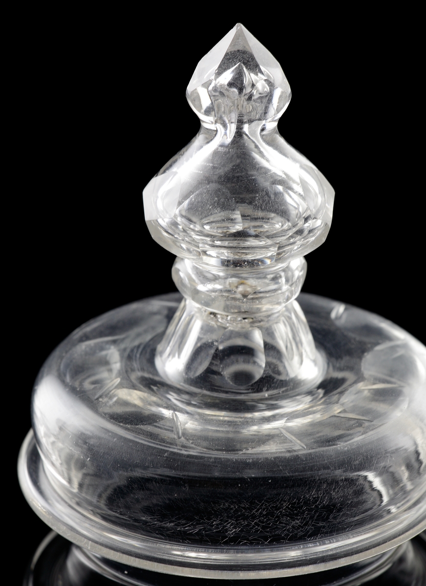 Pokal av glas, med lock. 
Slipat och graverat mönster med kungligt spegelmonogram: "FR"* i kartusch under krona.

*"FR" (Fredericus Rex= Fredrik I av Sverige, reg. 1720-1751).