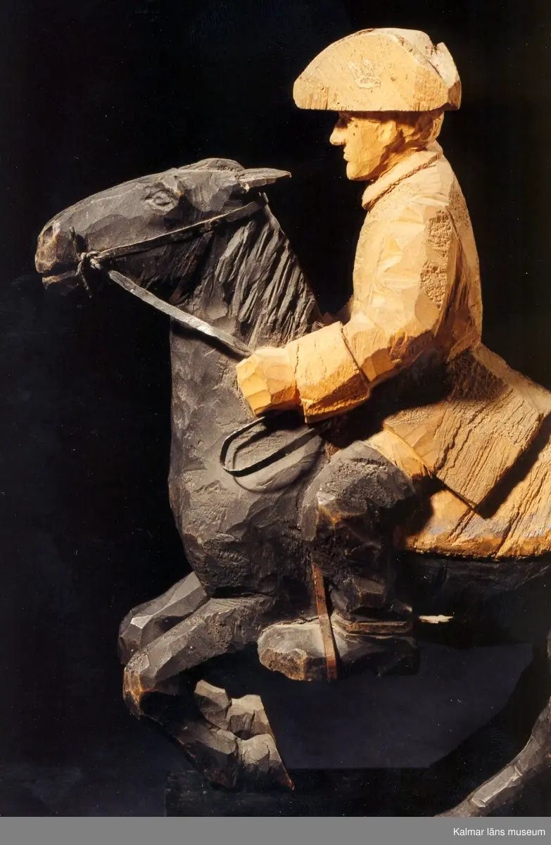 KLM 39255:31. Skulptur, av trä, bemålad. Ryttare till häst, Karl XII. Figur stiftad mot träplattan. Ryttaren har uniformsrock och hatt av karolinermodell samt bär sporrar. Hästen är utrustad med träns och betsel i svartmålad plåt, smidda stigbyglar i koppar samt randmålad sadel i blått och bronsfärg(?). Signerad, H.C. På hästens ländrygg samt på plattans ovansida. Inristad kursiverad text på plattans långsidesfront, E. Tegners tex: Högbarmad, smärt, gullhårig, en ny Aurora kom, Från Kämpe tjugoårig hon vände ohörd om. Datering, omkring 1930. Tillverkad av Helge Rugland, f. Carlsson.
Figuren hör samman med KLM 39255:17 Aurora Königsmarck, vilka utgör en figurgrupp, benämnd, Karl XII och Aurora Königsmarck.