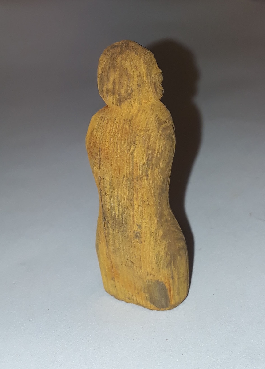 Troligen spelpjäs av trä i form av en kvinnofigur. Troligen en schackpjäs.