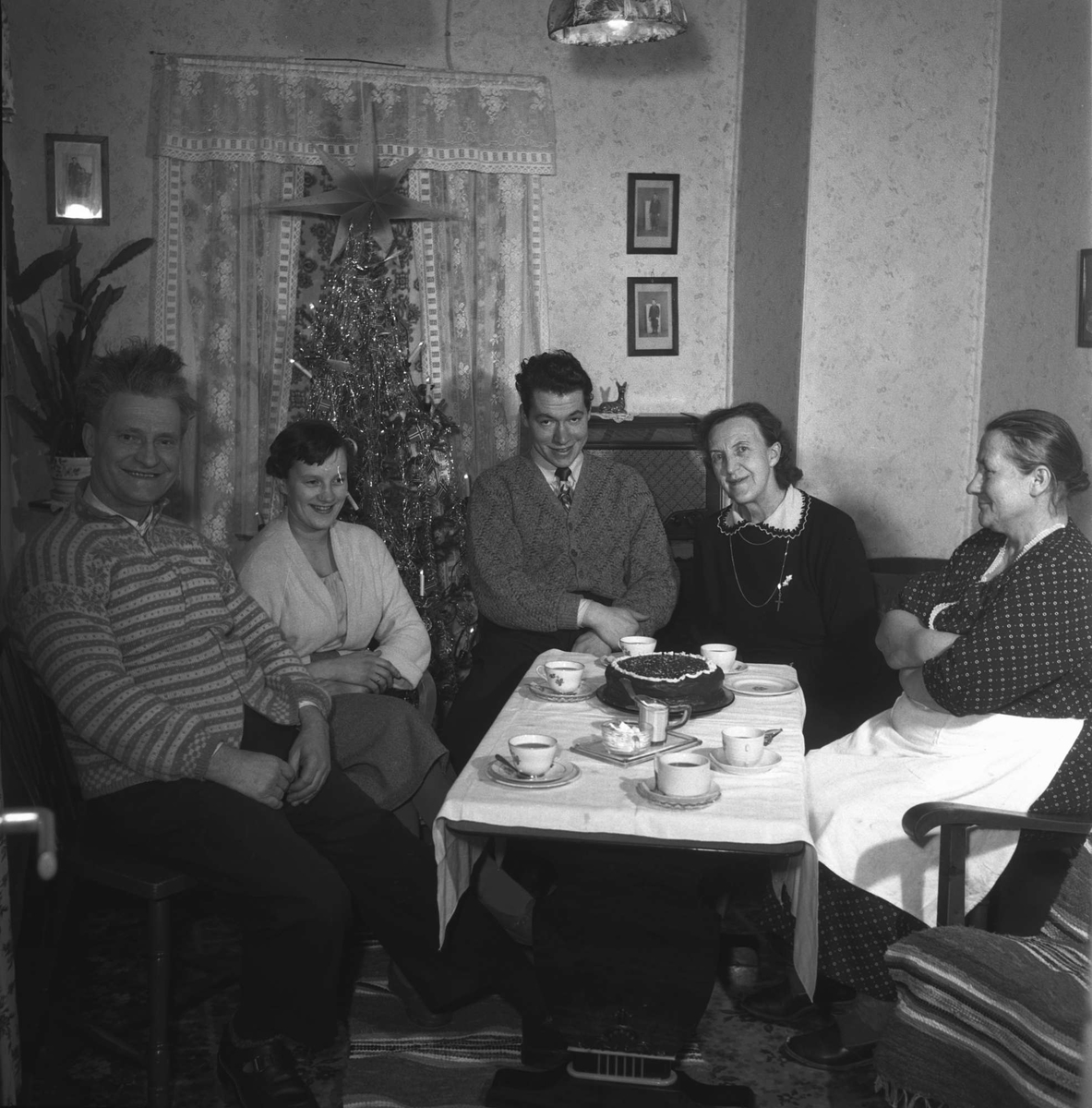 Kvinner og menn samlet for kaffe og kake. Juletre i bakgrunnen.