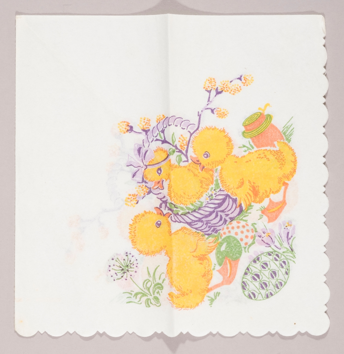 En andunge sitter i en kurv med grener med "gåsunger". To andunger står på en gressplen med påskeegg, en løvetann blomst, krokus og en tønne.