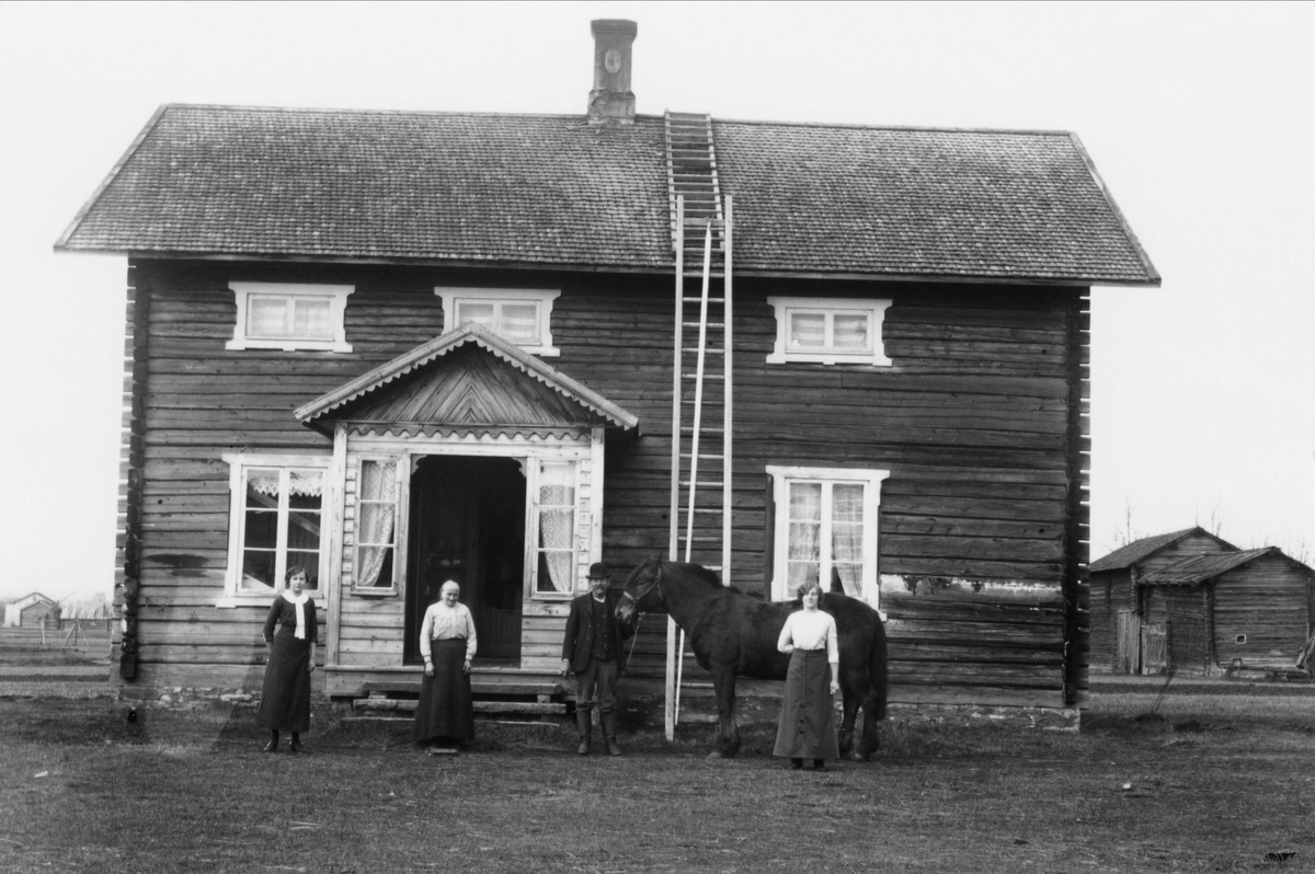 Tre kvinnor, en man med häst utanför bostadshus