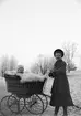 Ung kvinna i park, med sannolikt Roland Liljefors i vagnen